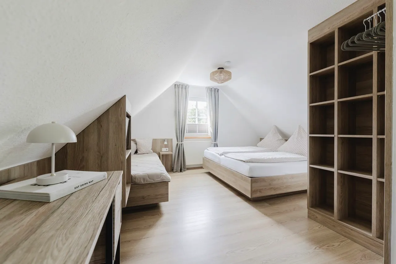 Bedroom under the sloping roof of the holiday home with beds, a desk and open shelving