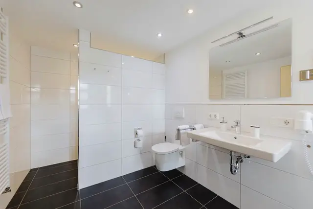 Weiß gefliestes Badezimmer der Ferienwohnung mit Dusche
