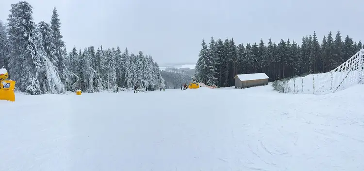 Verschneite Piste mit Schneekanone und Wald im Skiliftkarussell Winterberg